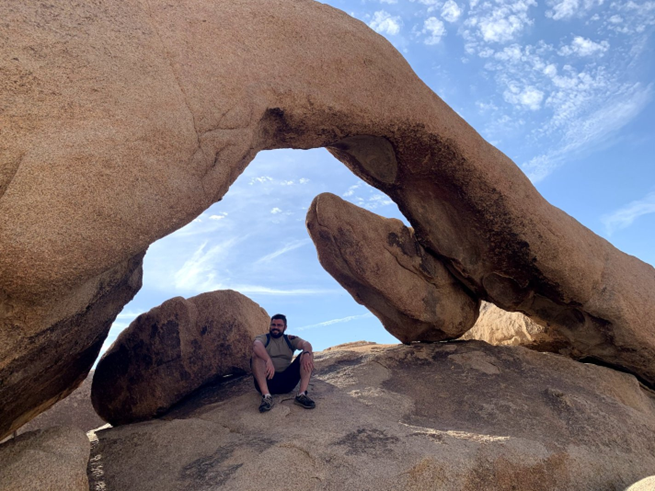 Morgan's husband sittin g under a rock arch in the desert